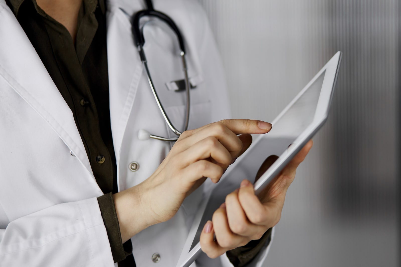 A clinician in a white coat holding a tablet — a patient's record, in careful hands.